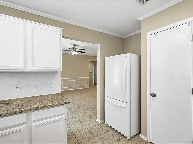 Kitchen featuring freestanding refrigerator, crown molding, white cabinets, light stone counters, and light tile patterned floors