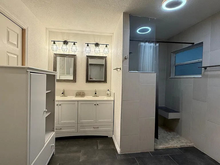 Updated bathroom with a double-sink vanity, ample storage, and a tiled walk-in shower with glass panel and built-in seat.