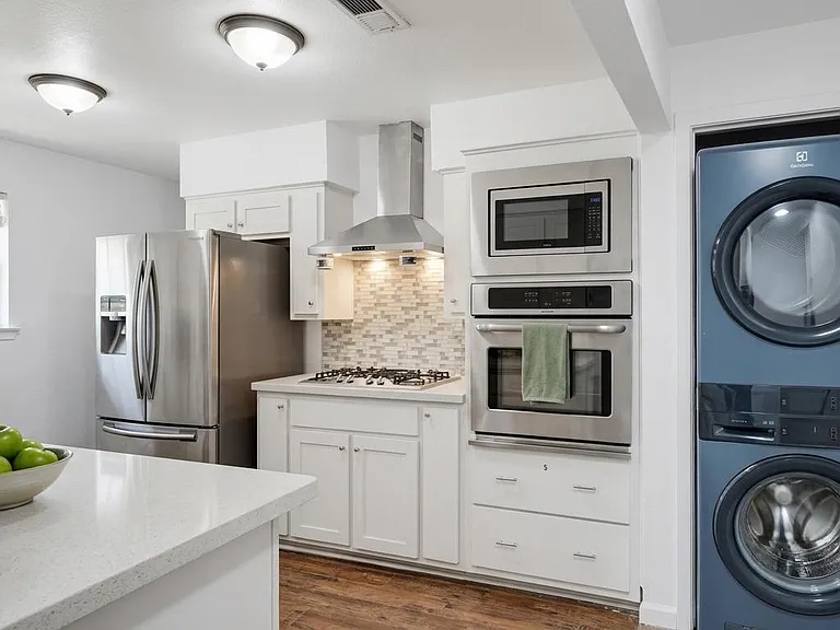 Well-appointed kitchen with quartz counters, stainless appliances, gas range, tile backsplash, and in-unit stacked laundry.