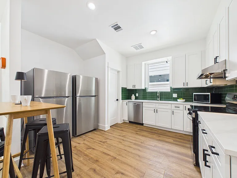 Well-equipped kitchen with ample white cabinetry, green tile backsplash, and stainless appliances plus an eat-in table.