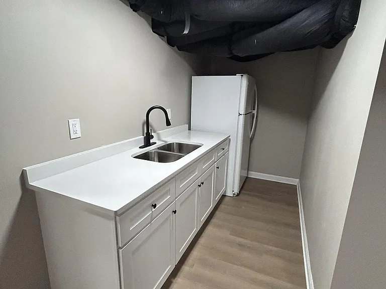 Compact kitchenette with generous counter space, double-basin sink, lower cabinets, and a full-size refrigerator.