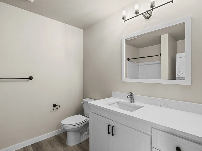 Modern apartment bathroom with quartz vanity, white cabinetry, framed mirror, updated lighting, and luxury vinyl plank flooring. Modern apartment bathroom with quartz vanity, white cabinetry, framed mirror, updated lighting, and luxury vinyl plank floorin