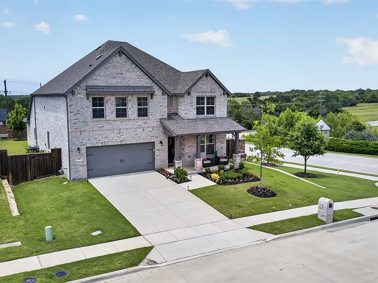 Stone-brick facade home featuring a covered front porch, an attached two-car garage, established front landscaping, and a concrete driveway