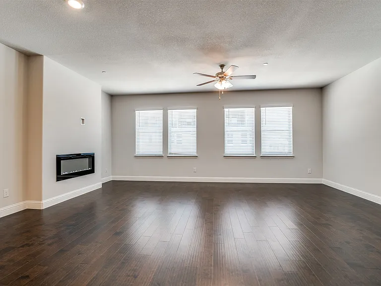 Spacious room featuring wood-finish flooring, a wall-mounted electric fireplace, multiple windows with blinds, a ceiling fan with integrated lighting, and recessed lighting