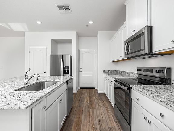 The kitchen has stainless steel appliances and plank flooring,