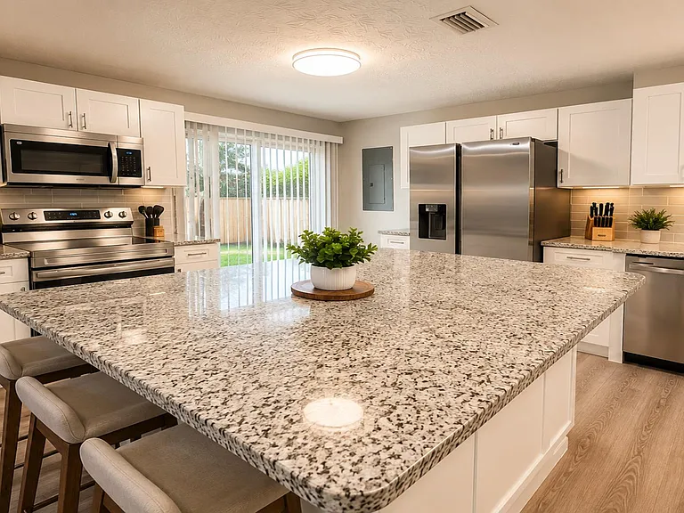 Spacious kitchen with a large granite island, stainless steel appliances, and ample cabinet storage plus backyard access.