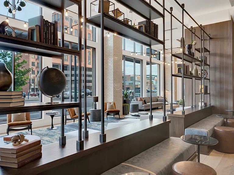 Chic modern lounge area with stylish decor, elegant shelving, and large windows offering city views, creating a warm and inviting atmosphere.