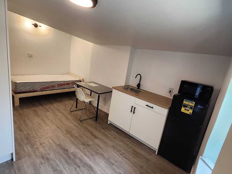 Studio view from living room with fridge, microwave, sink, table and bed.