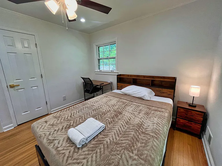 Furnished bedroom with a full bed, nightstand lighting, dedicated desk area, hardwood floors, and a window for fresh air.