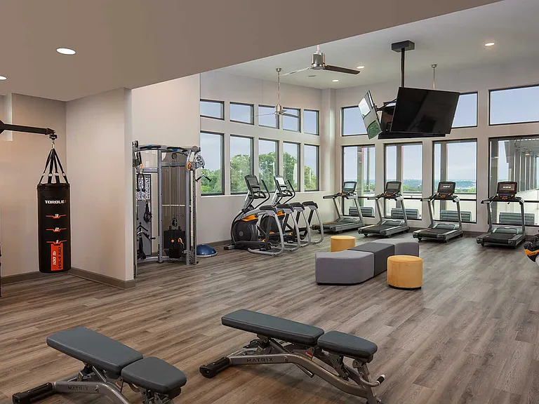 alt="fitness center with tvs, treadmills, medicine balls, boxing bag, and other various equipment"