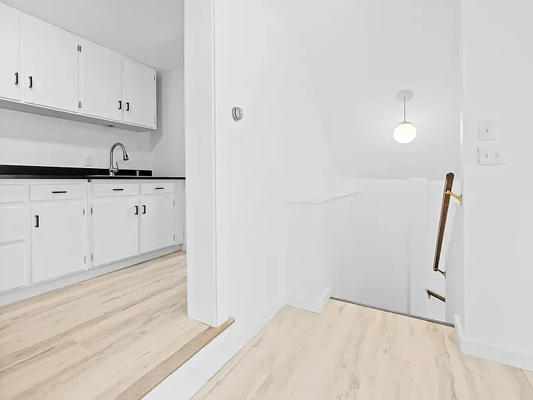 Kitchen opening & Stairs to Second Floor. The white Kitchen is well lit with dimming track lights. The stairs are well lit, too.