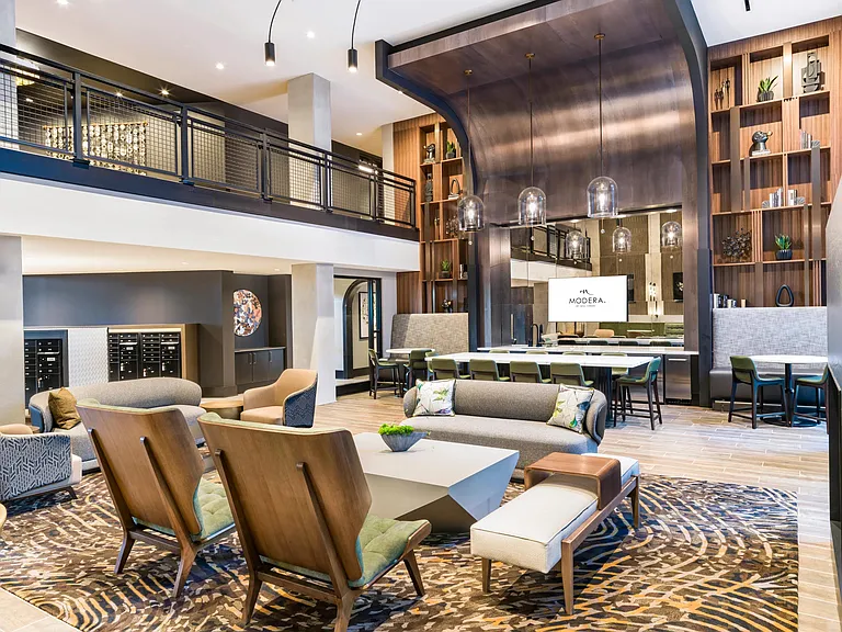 Double-height community lounge with layered seating, a shared kitchen, and warm wood details designed for conversation, hosting, and everyday gathering.