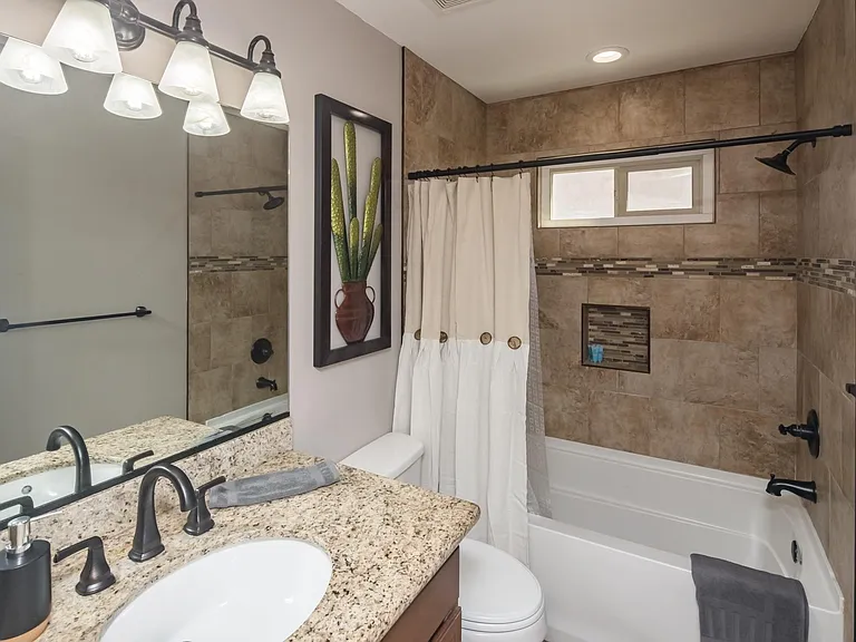 Updated bathroom featuring granite countertops, tiled tub/shower surround with decorative accent band, and modern fixtures.
