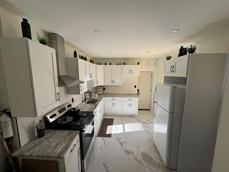 Galley kitchen with ample shaker cabinetry, subway-tile backsplash, stone-look counters, and full-size appliances.