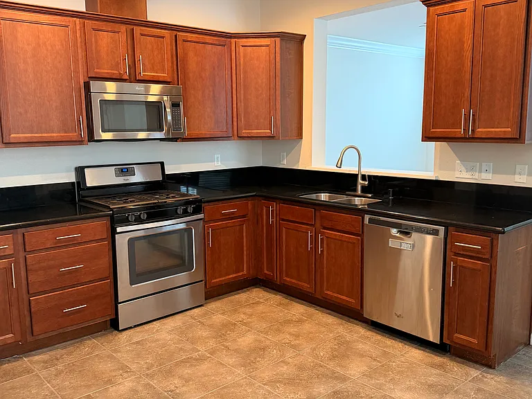 Kitchen with gas range, stainless steel appliances, walnut cabinetry, and granite countertops