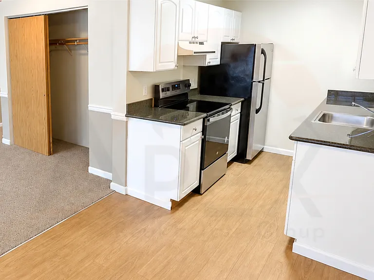 Compact kitchen with white cabinetry, dark countertops, full-size appliances, and nearby closet storage.
