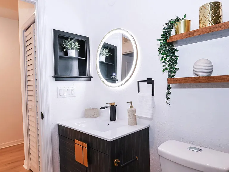 The stylish bathroom has an LED lit mirror with digital display and tasteful decorations.