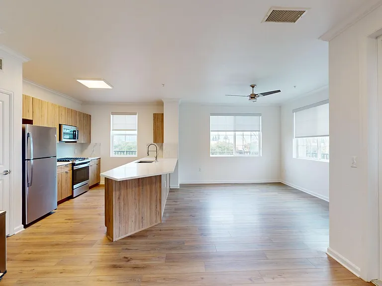 Apartment kitchen with stainless steel appliances, dining and living room with wood style floor.