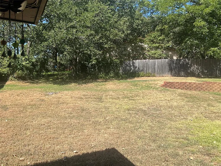 Expansive backyard featuring a wood fence, mature trees, and a terraced garden bed