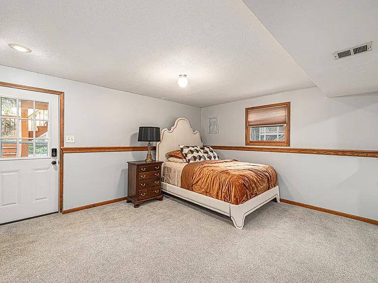 Enjoy a large, airy basement bedroom with simple yet elegant design, complete with a table, cabinet, and bedside lamp for comfort and style.