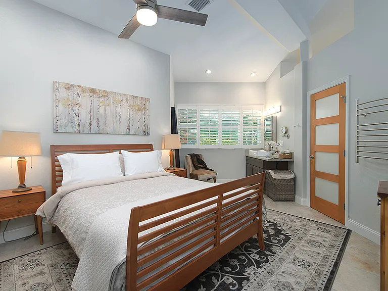 Primary bedroom with a large queen size bed. The room includes a vanity and a view to the outdoor space.