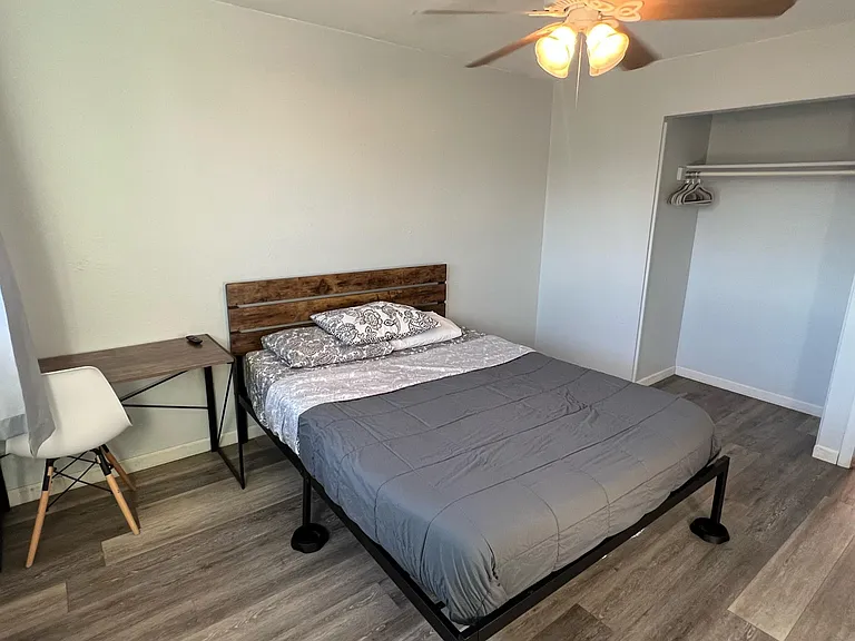 Furnished bedroom with a bed, desk workspace, ceiling fan, and an open closet for convenient everyday storage.