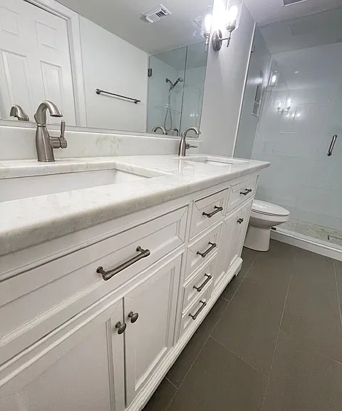 newly tiled bath with double sink credenza, marble counter, and glass shower enclosure