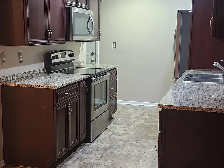 Galley kitchen with recessed, dimmable, motion lighting. Granite Counters, Stainless Steel Sink. Cherry cabinets