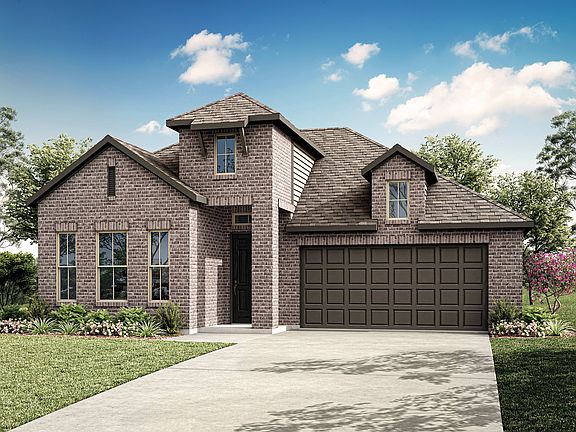 A two-story brick house with a gabled roof, surrounded by lush greenery and a clear blue sky with fl