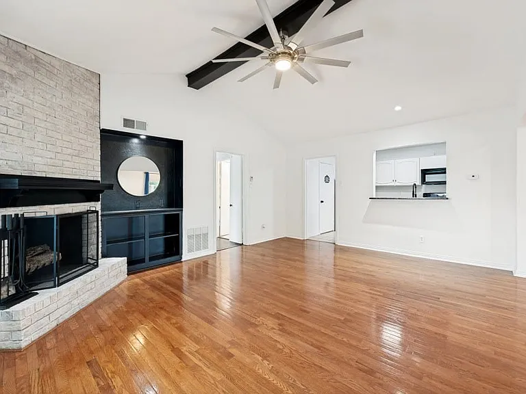 Spacious living area featuring wood-finish flooring, a white brick fireplace with a black mantel, and a built-in shelving unit
