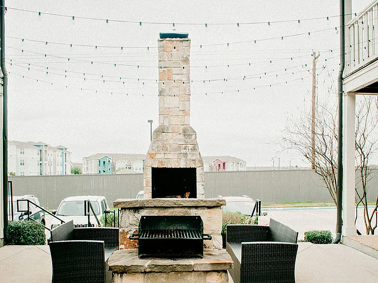 Relax in this charming outdoor patio featuring a cozy stone fireplace and stylish seating.