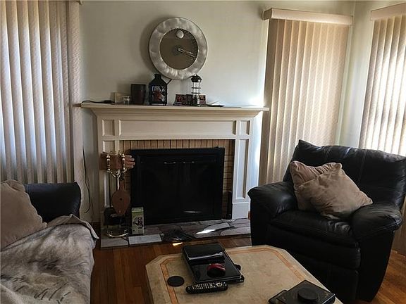 The pretty Living Room has a log burning fireplace with mantel. Vertical blinds are on the many windows.