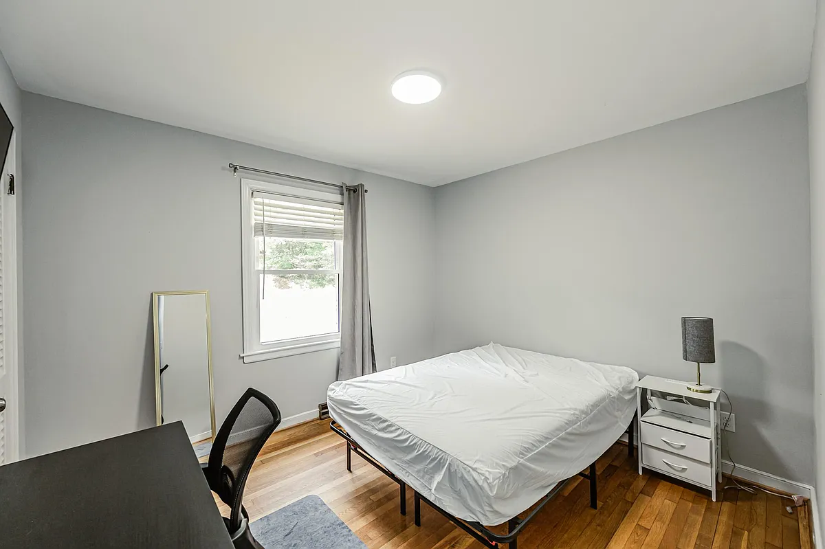 Private bedroom with hardwood floors, a window with blinds and curtains, and space for a bed plus a small work area. - Stratford Ct