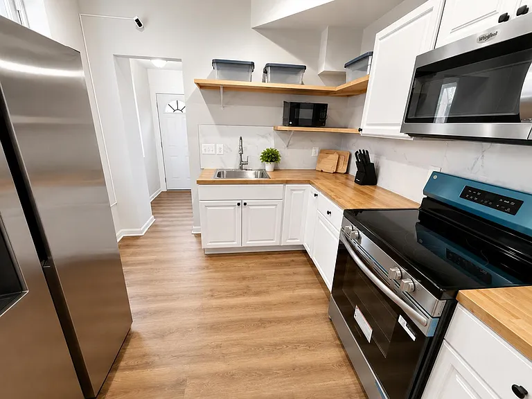 Efficient L-shaped kitchen with butcher-block counters, stainless appliances, open shelving, and a large sink workspace.