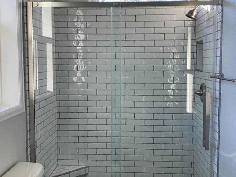 Spacious walk-in shower with subway tile, footrest, and built-in nook for toiletries.