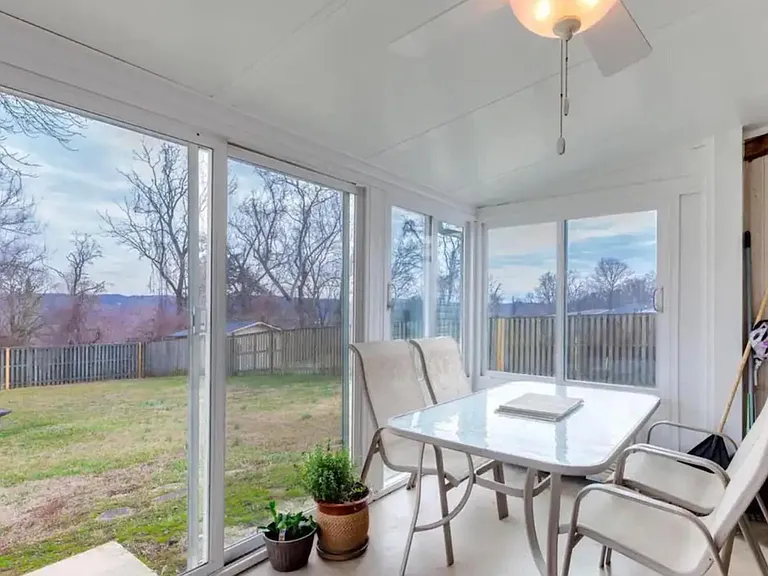 Enclosed sunroom with sliding glass walls, ceiling fan, and space for a small dining set overlooking the backyard.