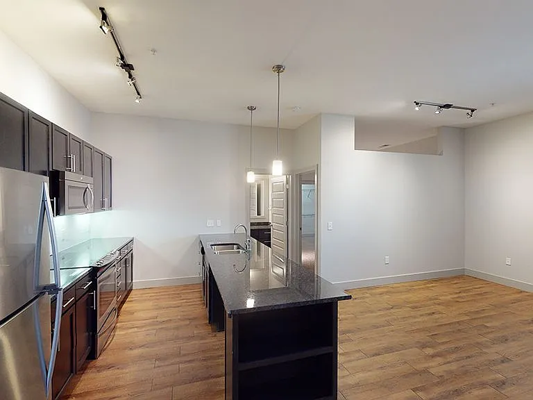 Apartment living room with wood-style flooring and kitchen peninsula (shown here). Kitchen island available in select homes.