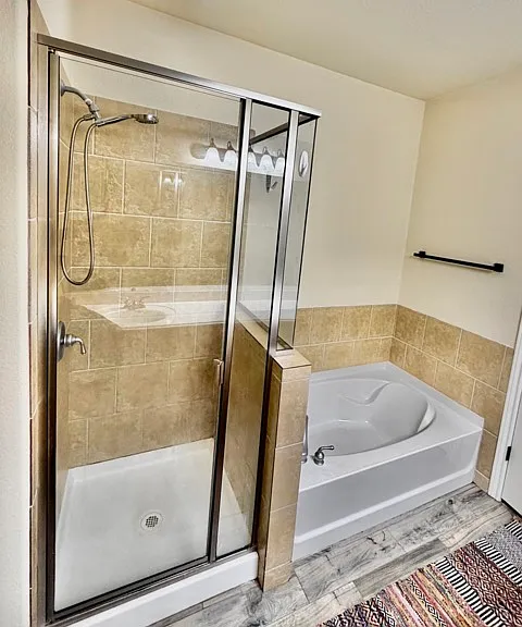 Primary bathroom with glass-enclosed walk-in shower and a deep soaking tub, tile flooring throughout