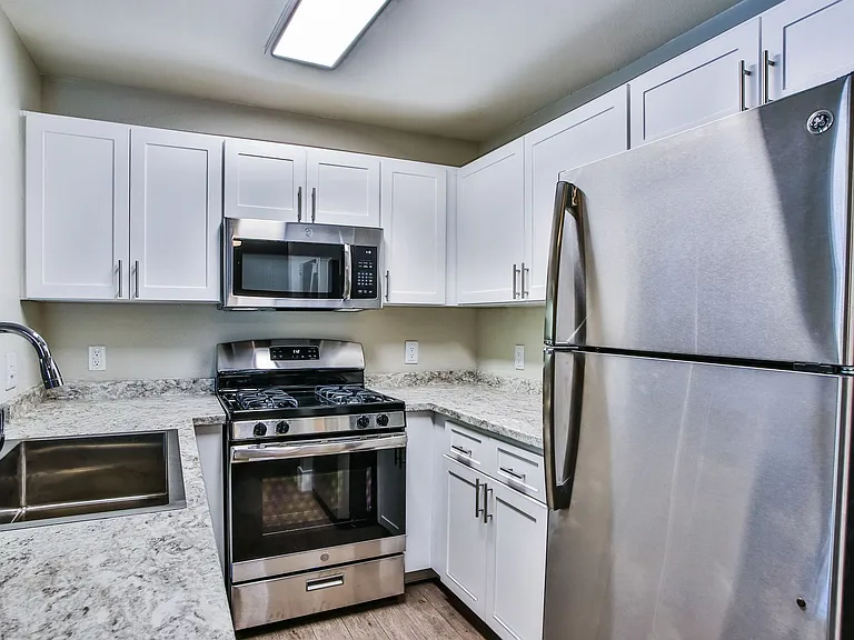 Stainless steel microwave and gas range with white shaker cabinets, granite counter, and large sink.
