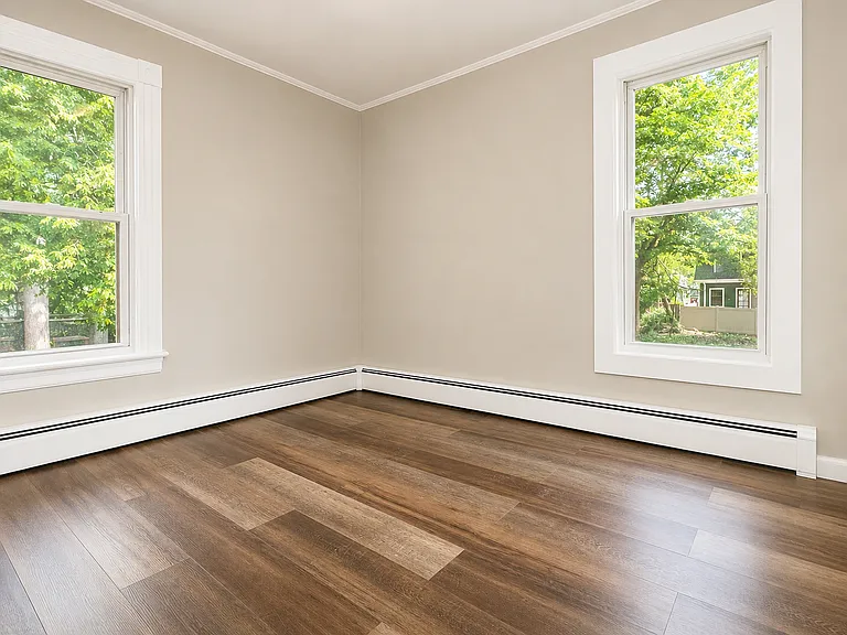Comfortable second bedroom with new flooring, neutral paint, and multiple windows.