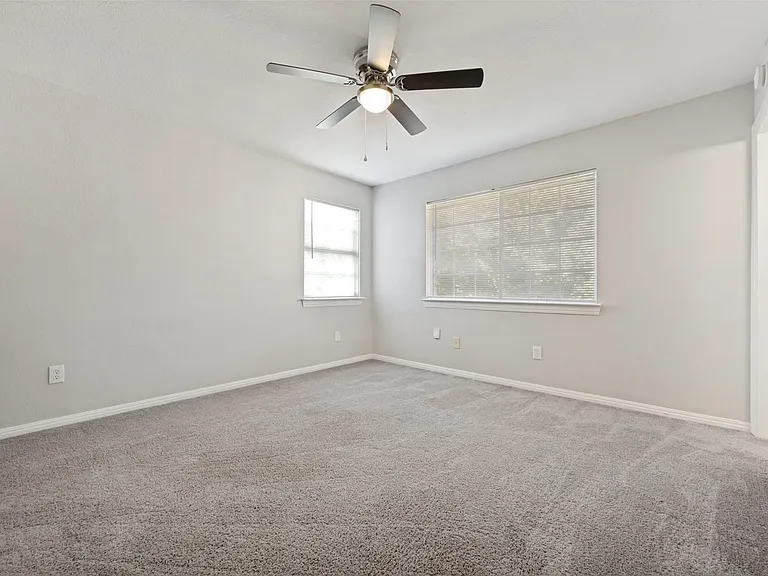 Spacious room featuring neutral carpeting, light-toned walls, and a ceiling fan with integrated lighting