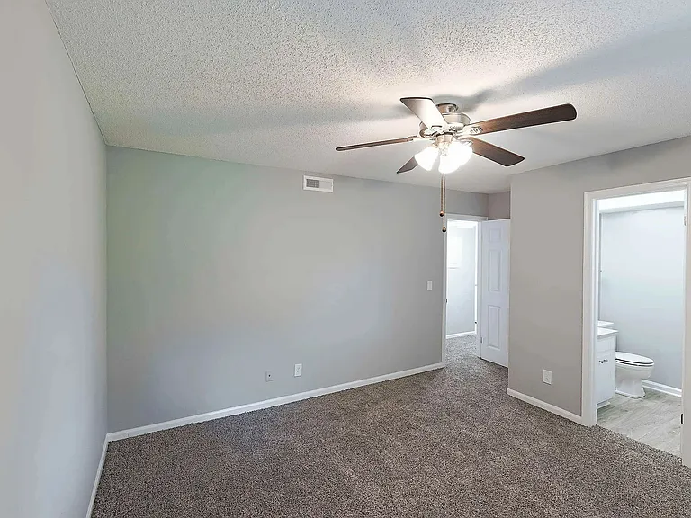 Spacious bedroom with plush carpeting, ceiling fan, and natural light