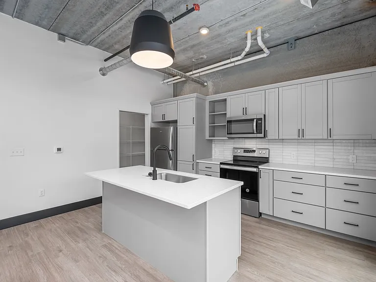 Modern open-concept kitchen with sleek countertops, stainless steel appliances, and stylish pendant lighting under an industrial ceiling. Modern open-concept kitchen with sleek countertops, stainless steel appliances, and stylish pendant lighting under an