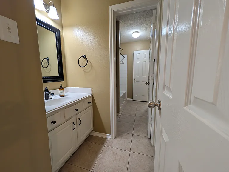 A smart, split-style bathroom featuring a shared central tub/shower room. One private vanity connects directly to Bedroom 2, while a second separate vanity is accessible via the main hallway to serve guest bedrooms.