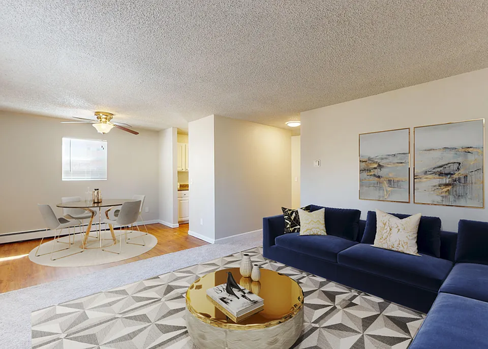 Inviting living room with a modern blue sofa, decorative pillows, and a chic round coffee table; adjacent to a cozy dining area with a ceiling fan and elegant table set, showcasing open-concept comfort.