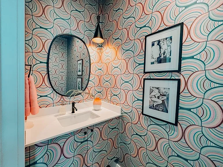 Powder room featuring a patterned wallcovering, a floating vanity with an integrated rectangular sink, a matte black wall-mounted faucet, and a black framed oval mirror