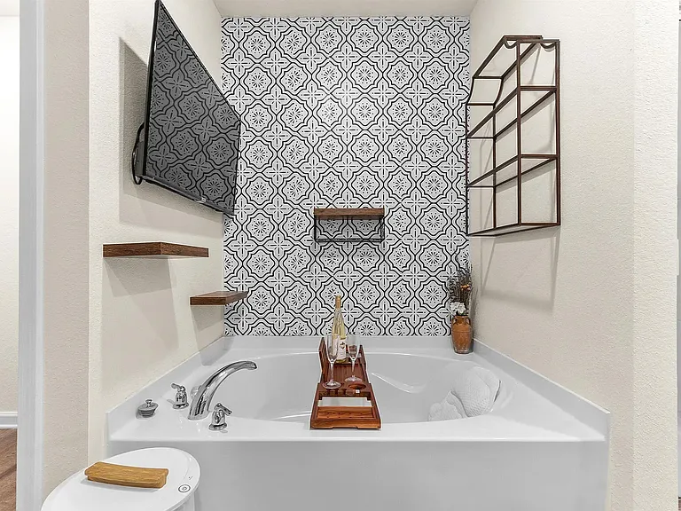 Unwind in a spacious master bedroom featuring a gorgeous accent wall and ample natural light. The attached master bath is a true oasis, complete with a deep soaking tub, a separate shower, a beautiful modern accent wall, and shelving.
