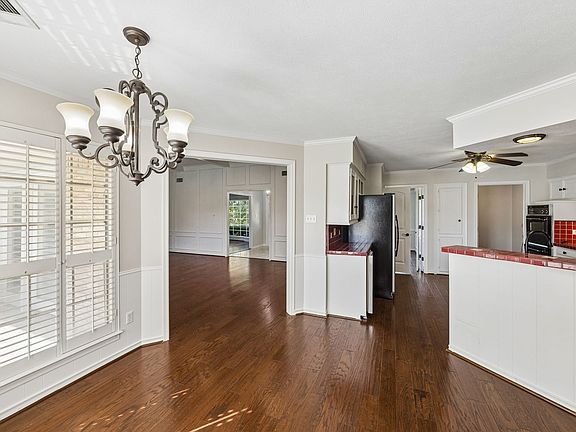 Wood-finish flooring throughout, with a decorative chandelier, white plantation shutters, and a kitchen featuring red tile accents