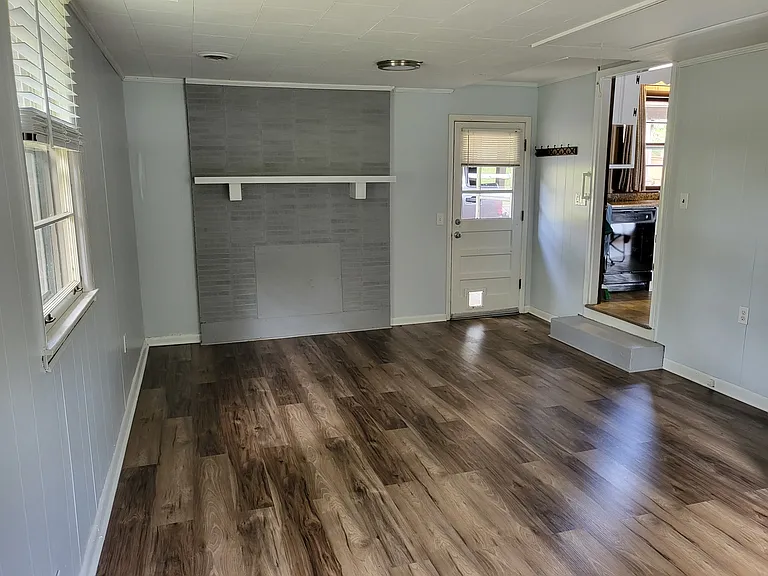 Bonus room with new floors and closed up fireplace. You can see the main entrance to the house via the back door and turn left into the kitchen.