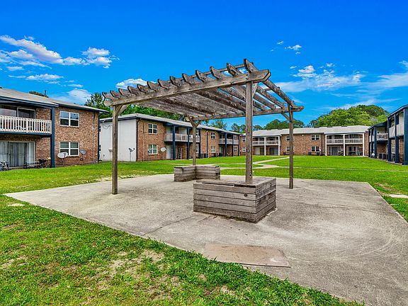 Charming apartment complex courtyard with a rustic wooden pergola, lush green lawns, and cozy balconies overlooking the space.